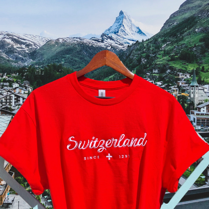 <img src="switzerland-embroidered-red-shirt.jpg" alt="Swiss heritage red shirt with intricate 'Switzerland Since 1291' embroidery">